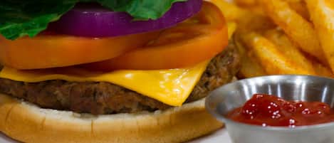 A hamburger with lettuce, tomato, and cheese, served with French fries and a small container of ketchup.