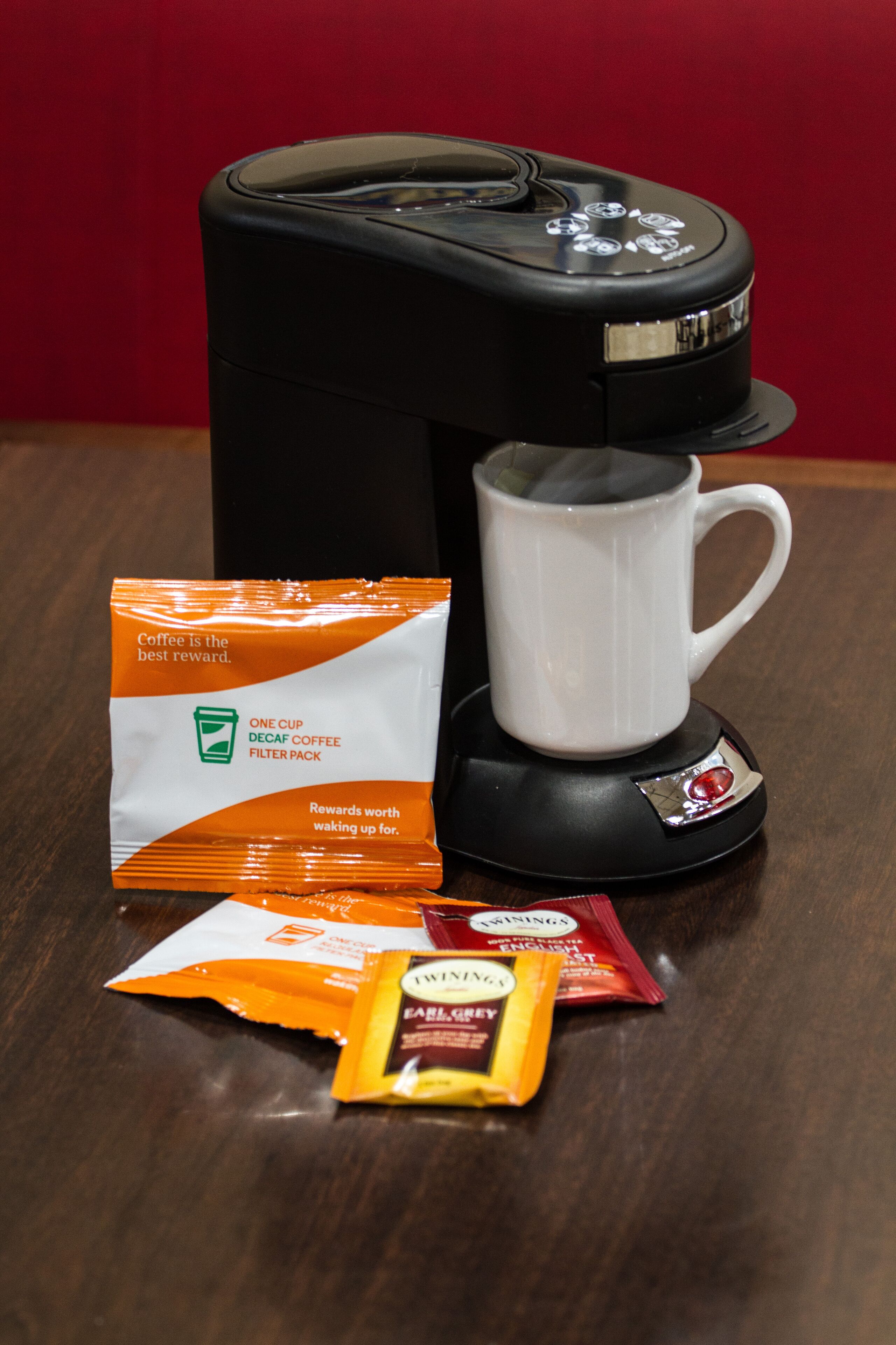 Een koffiezetapparaat met een mok, een pakje decaf koffiefilters en een zakje Twinings Earl Grey thee.