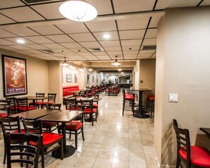 A spacious restaurant with multiple tables and booths, featuring a tiled floor and a high ceiling with recessed lighting.