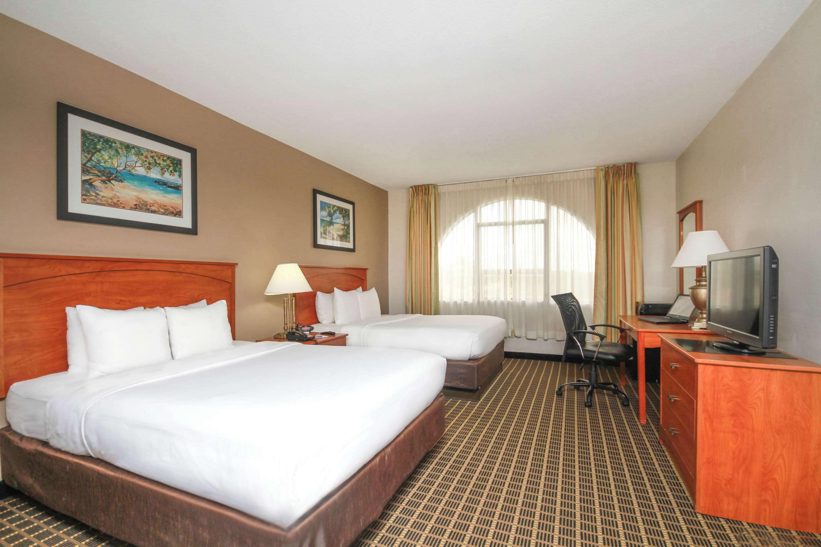 A hotel room with two beds, a desk with a television, and a chair.