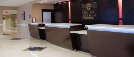 Zona de recepción de un hotel con diseño moderno, que incluye un mostrador de recepción, un área de descanso y un letrero de Clarion Inn & Suites.
