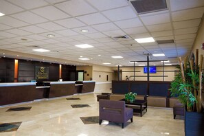 A hotel lobby with a reception desk, seating area, and a large screen.