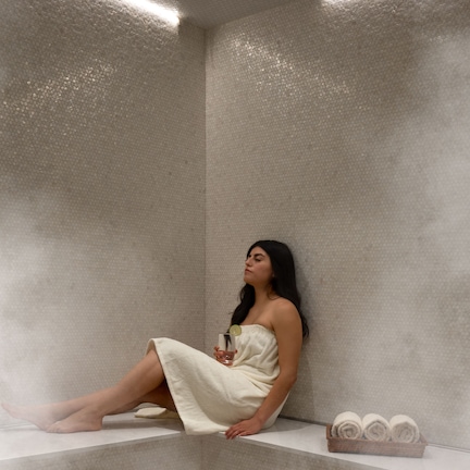 A person sitting in a steam room with a towel and a glass of water.