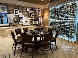 A dining area with a round table set for six, surrounded by leather chairs, with a wine rack filled with bottles to the right.