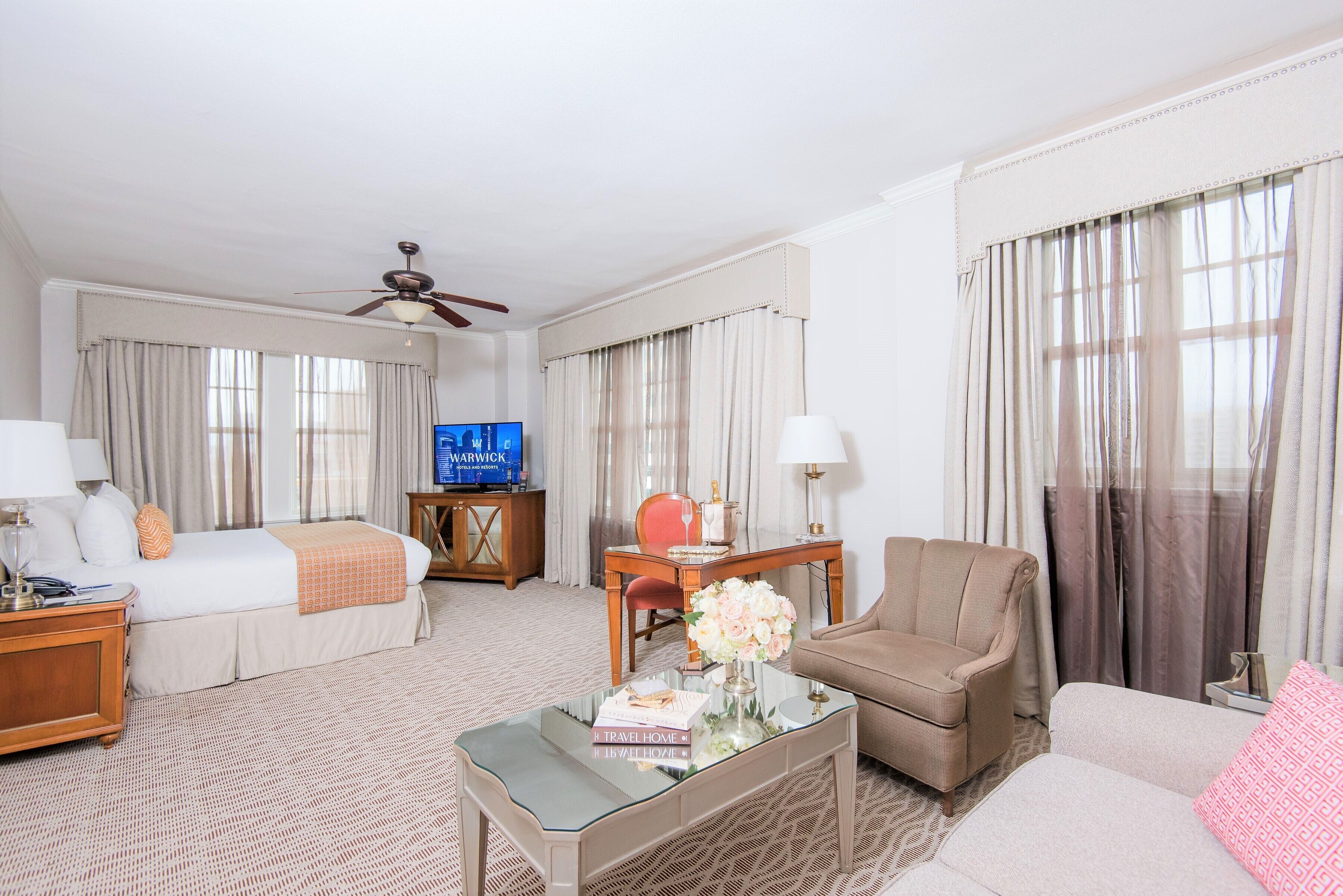 Une chambre d’hôtel avec un lit, un canapé, une table basse, une télévision et des rideaux.