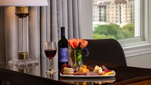 Een tafel met een fles wijn, een glas rode wijn, een bord kaas en crackers, en een vaas met bloemen.