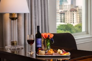A table with a wine bottle, a glass of red wine, a plate of cheese and crackers, and a vase with flowers.