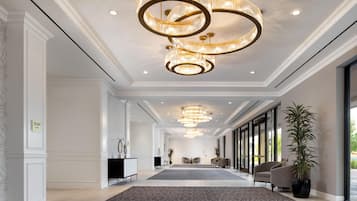 A spacious hotel lobby with a grand chandelier, a reception desk, and a large window offering a view.