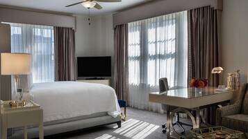 A hotel room with a bed, a desk, a chair, a television, and a ceiling fan.