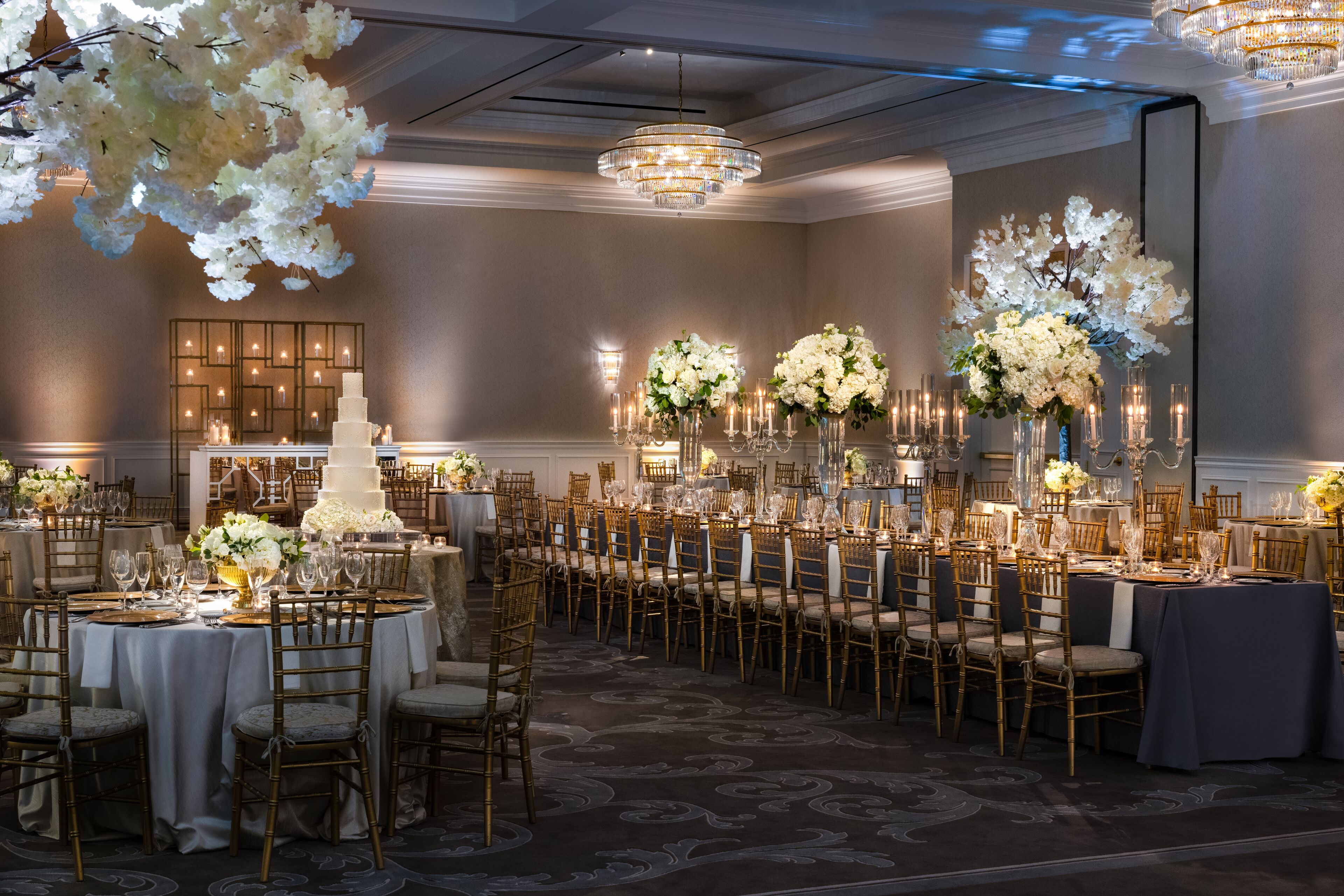 A banquet hall with round tables, chairs, and floral centerpieces.