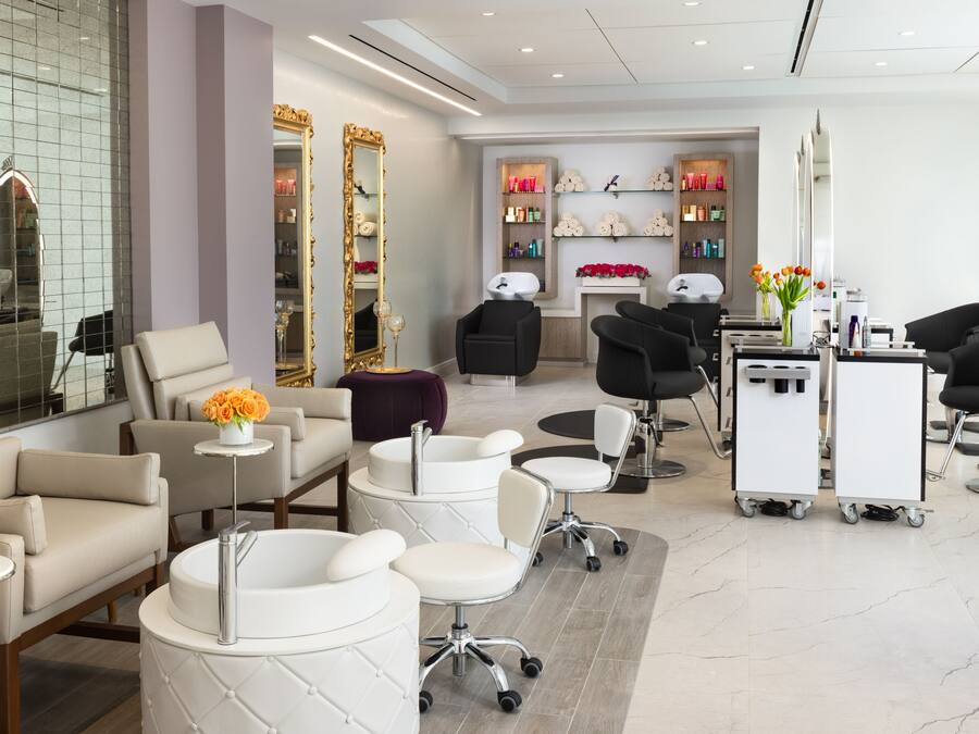 Um salão moderno com diversas áreas de estar, um balcão de recepção e exposição de produtos para cabelo.