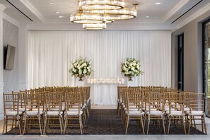 Formal event space with elegant seating, floral arrangements, and a high ceiling.