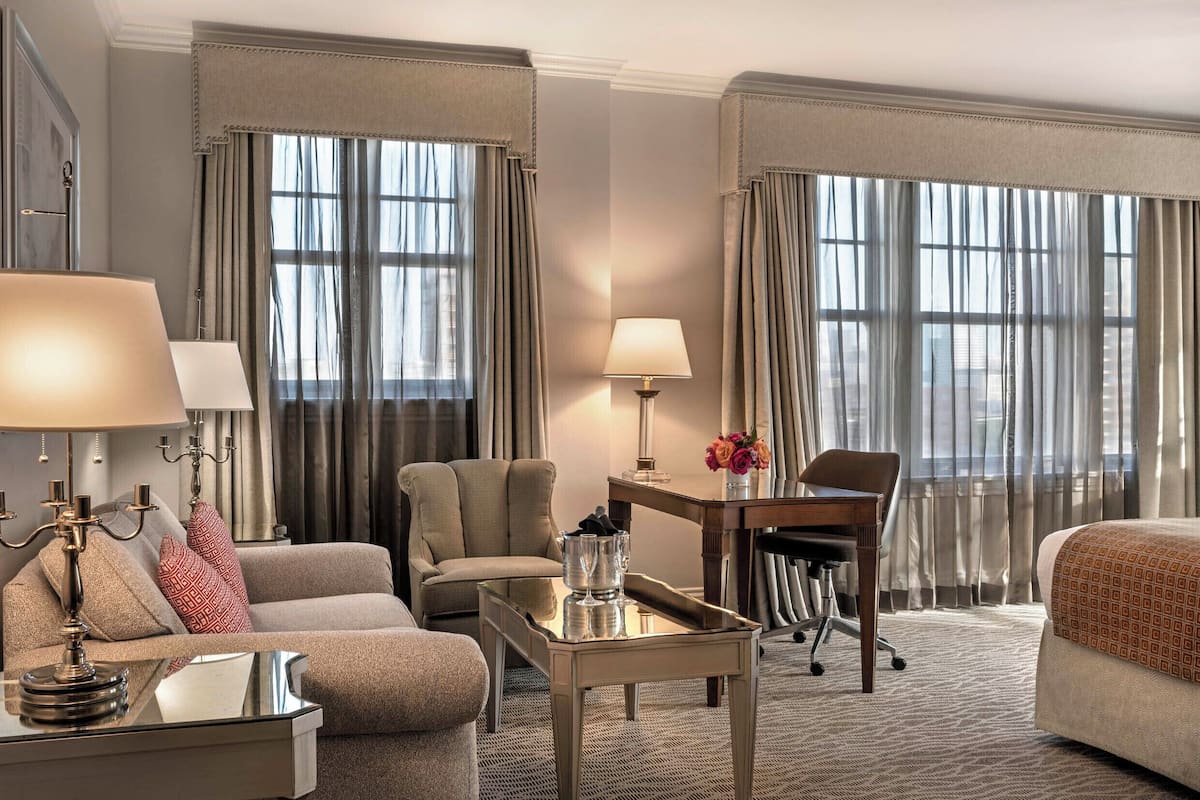 A hotel room with a sofa, armchair, desk, and a bed.