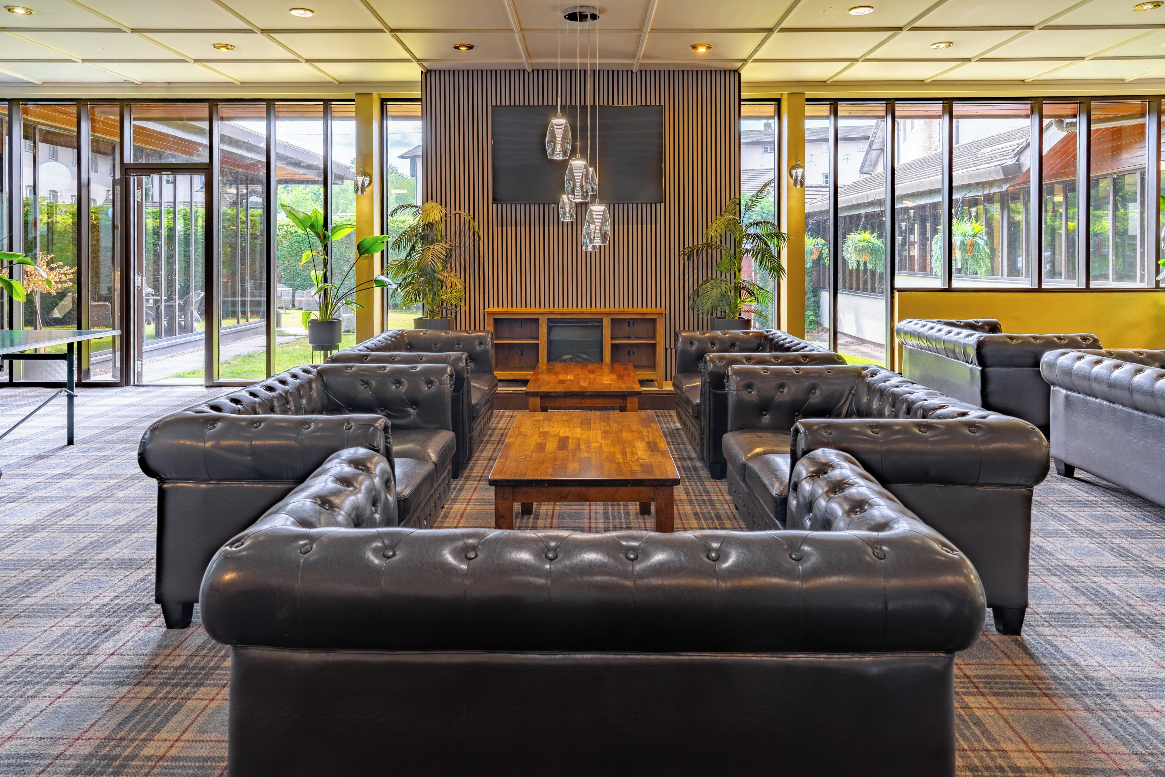 Een ruime lobby met leren banken, een houten salontafel en grote ramen met uitzicht op het omliggende landschap.