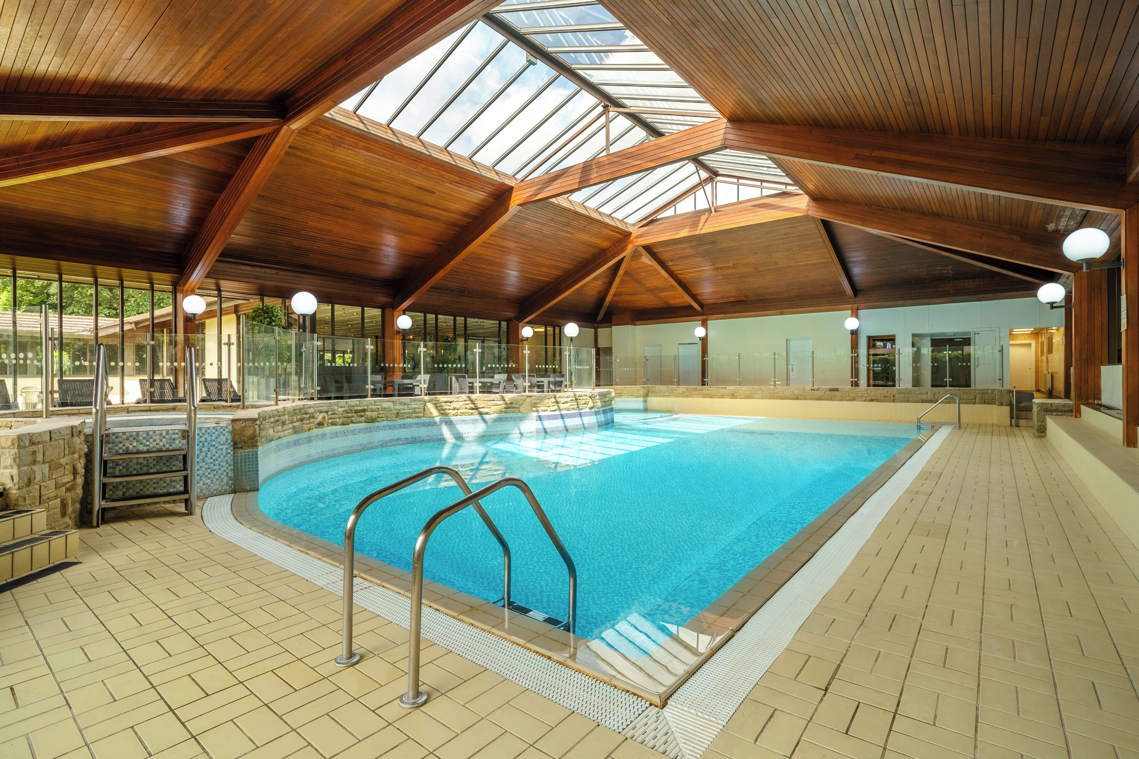 An indoor swimming pool with a wooden ceiling and glass walls.