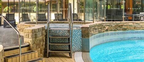 Une piscine avec un mur en pierre et des marches carrelées menant à l’intérieur.