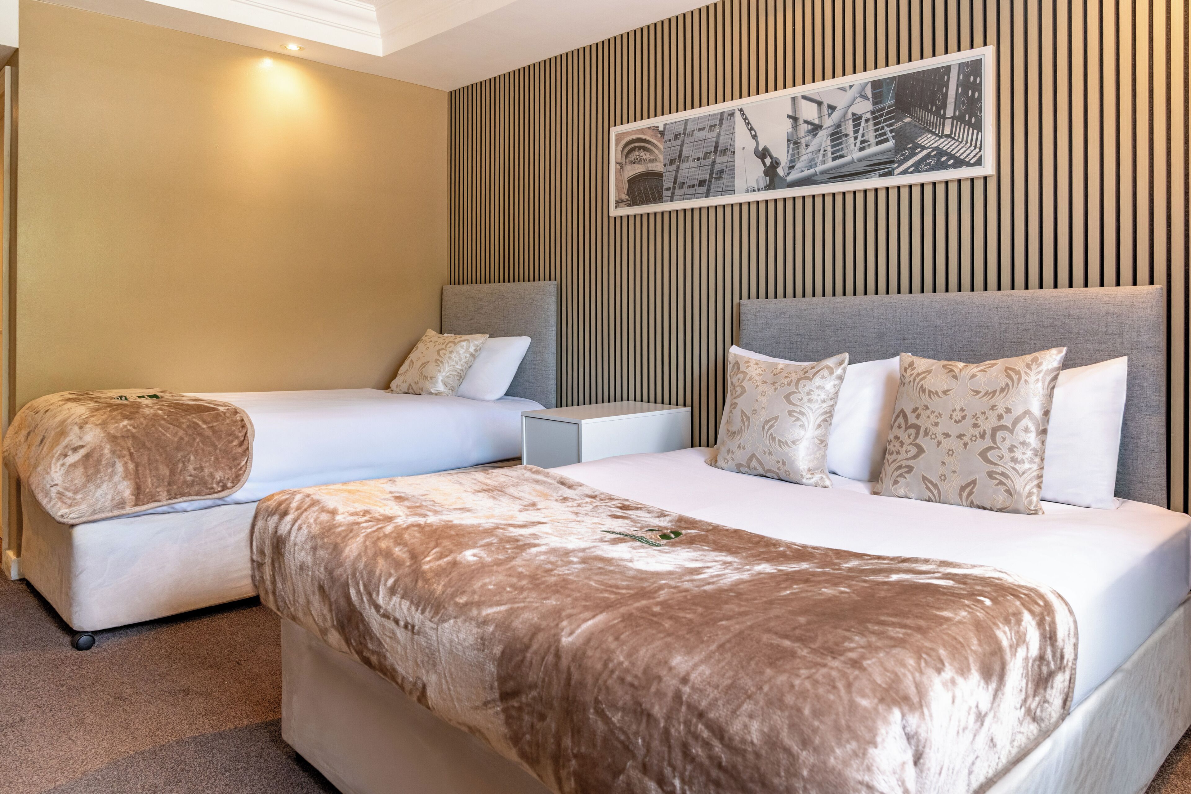 Une chambre d’hôtel avec deux lits, une table de chevet et un tableau accroché au mur.