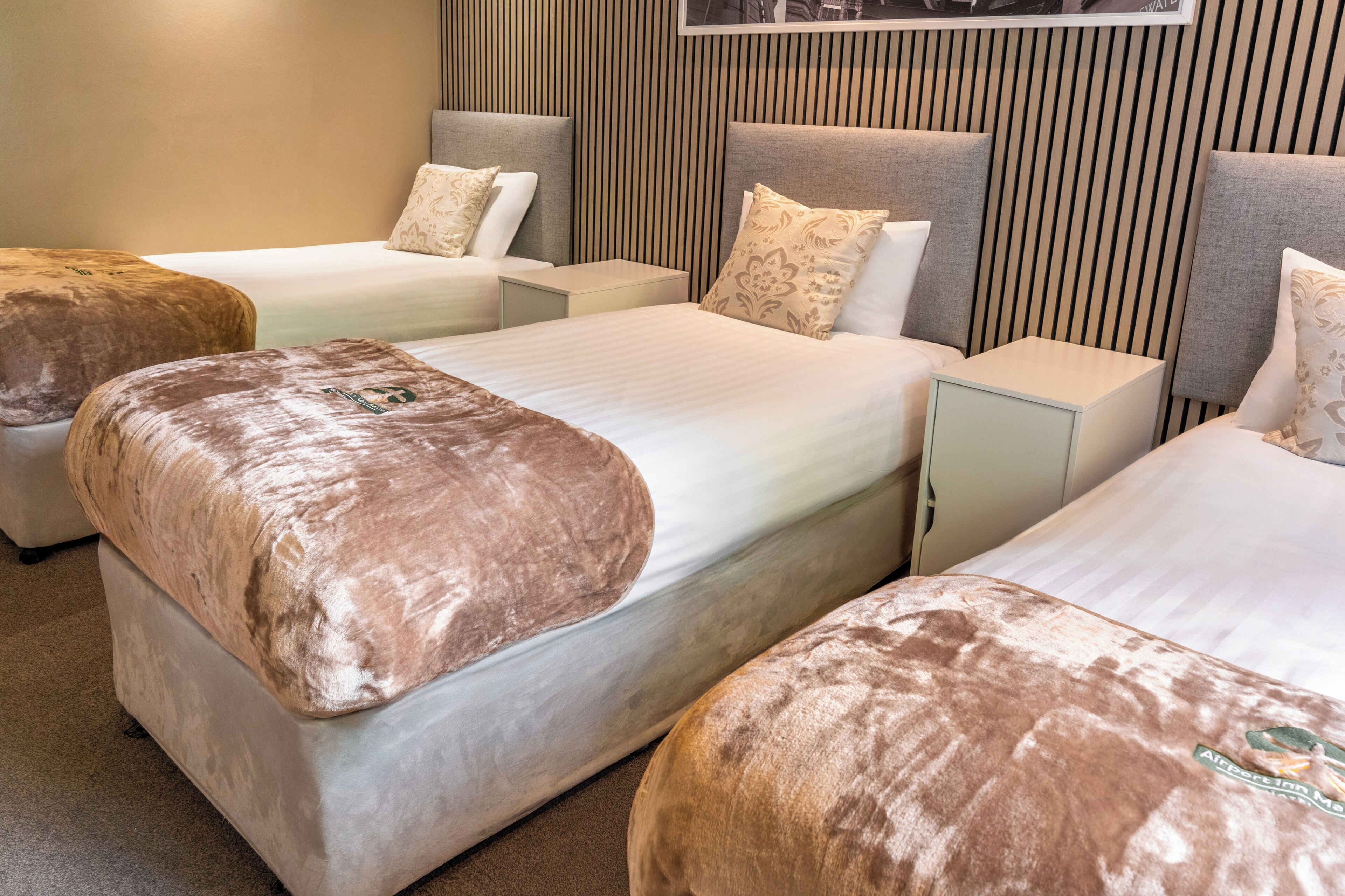 A hotel room with two beds, each with a headboard, a bedside table, and a pillow.