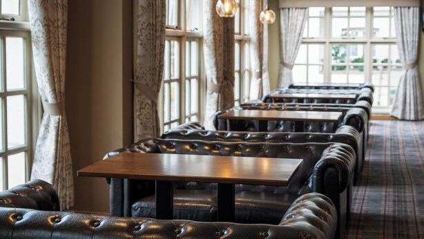 A restaurant with leather booths, wooden tables, and hanging pendant lights. - Britannia Airport Inn Manchester (Wilmslow)