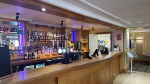 A bar area with a wooden counter, shelves of liquor bottles, and a coffee machine. - Britannia Airport Inn Manchester (Wilmslow)