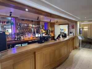 A bar area with a wooden counter, shelves of liquor bottles, and a coffee machine. - Britannia Airport Inn Manchester (Wilmslow)