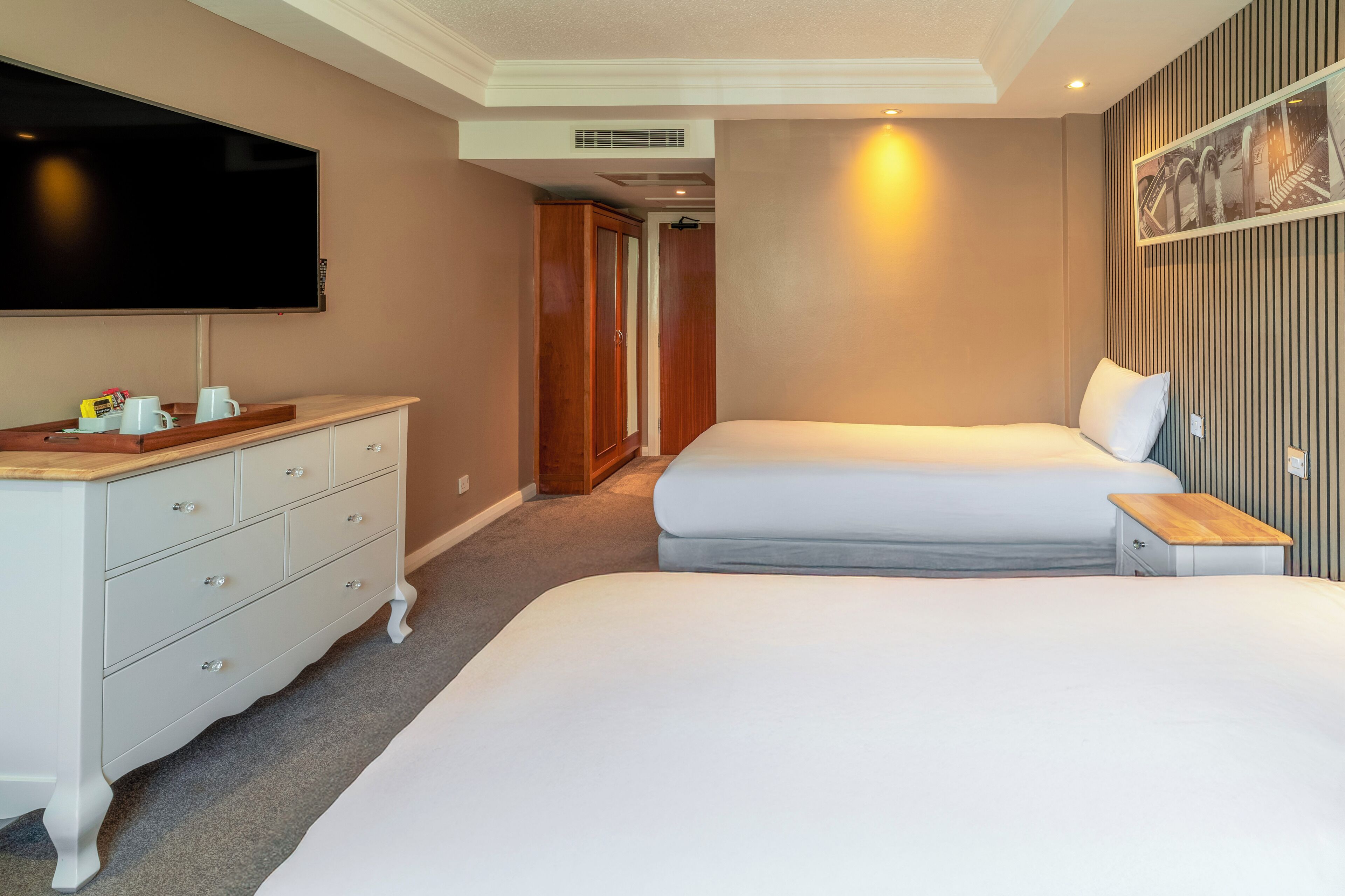 A hotel room with two beds, a TV, a dresser, and a small table.