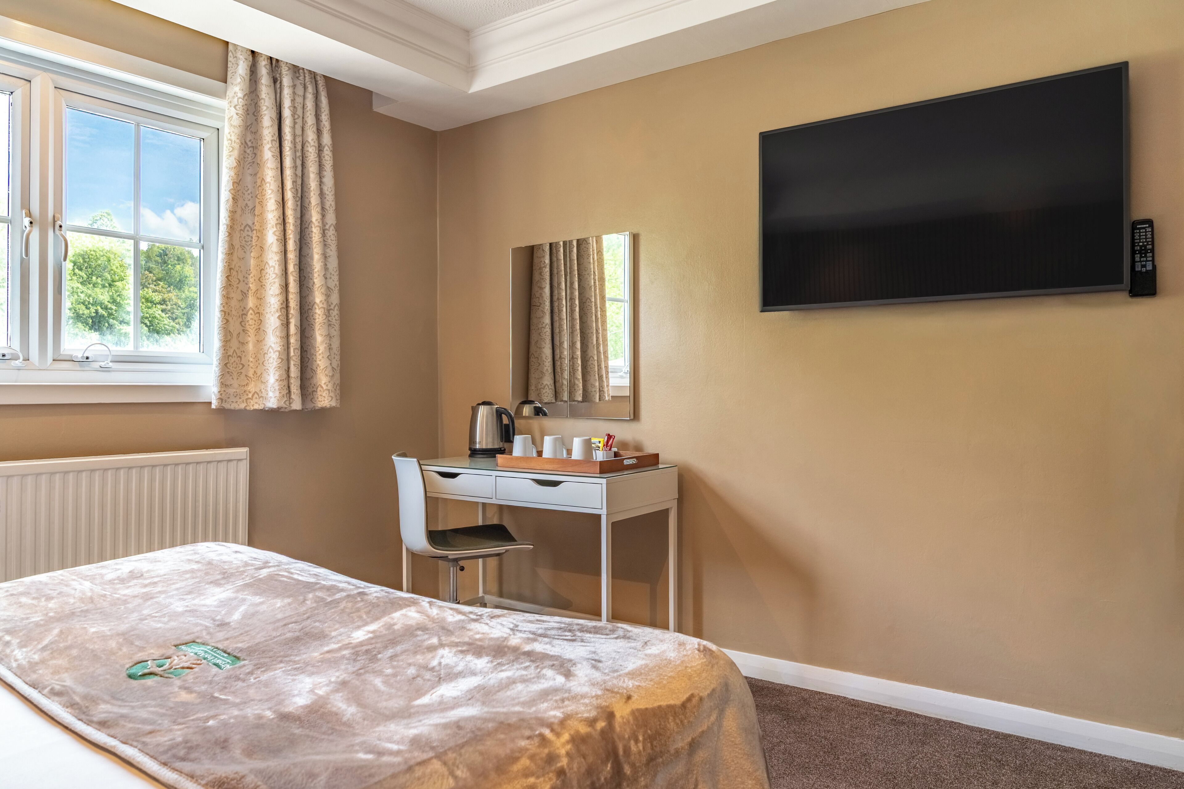 Una habitación de hotel con cama, un escritorio con silla, televisor y ventana con cortinas.