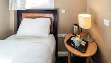 A hotel room with a neatly made bed, a bedside table with a lamp, a tray with toiletries, and a window with a curtain.