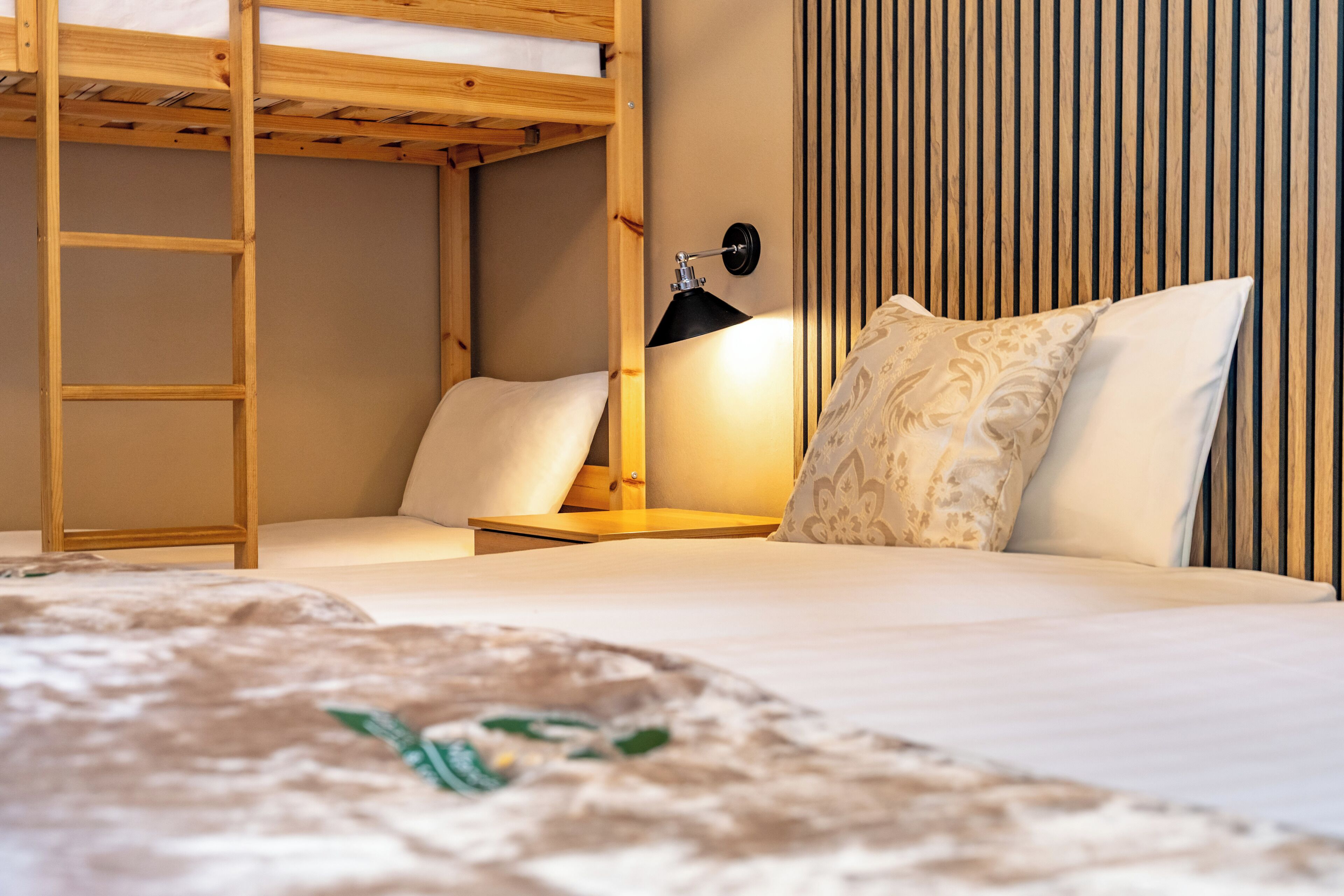 Una cama litera con escalera, una mesita de noche con lámpara y un cojín estampado.