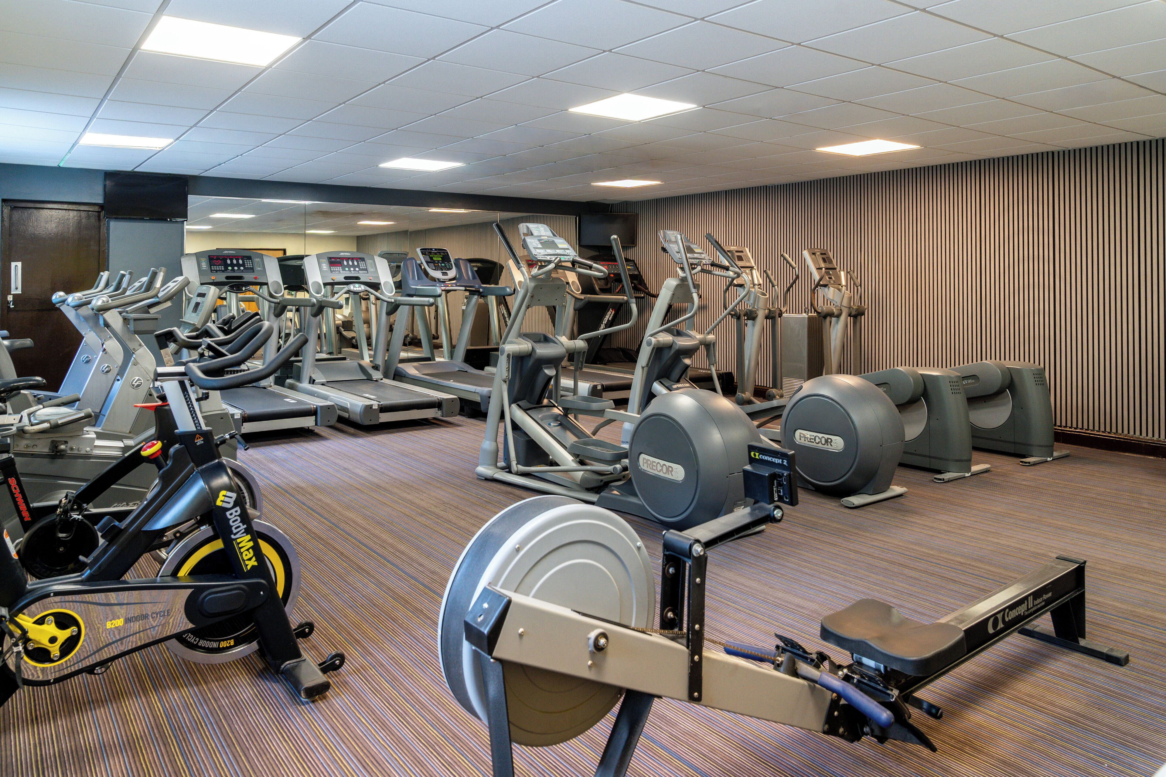 Un gimnasio con diversas máquinas de cardio, equipo de entrenamiento con pesas y un espejo grande.