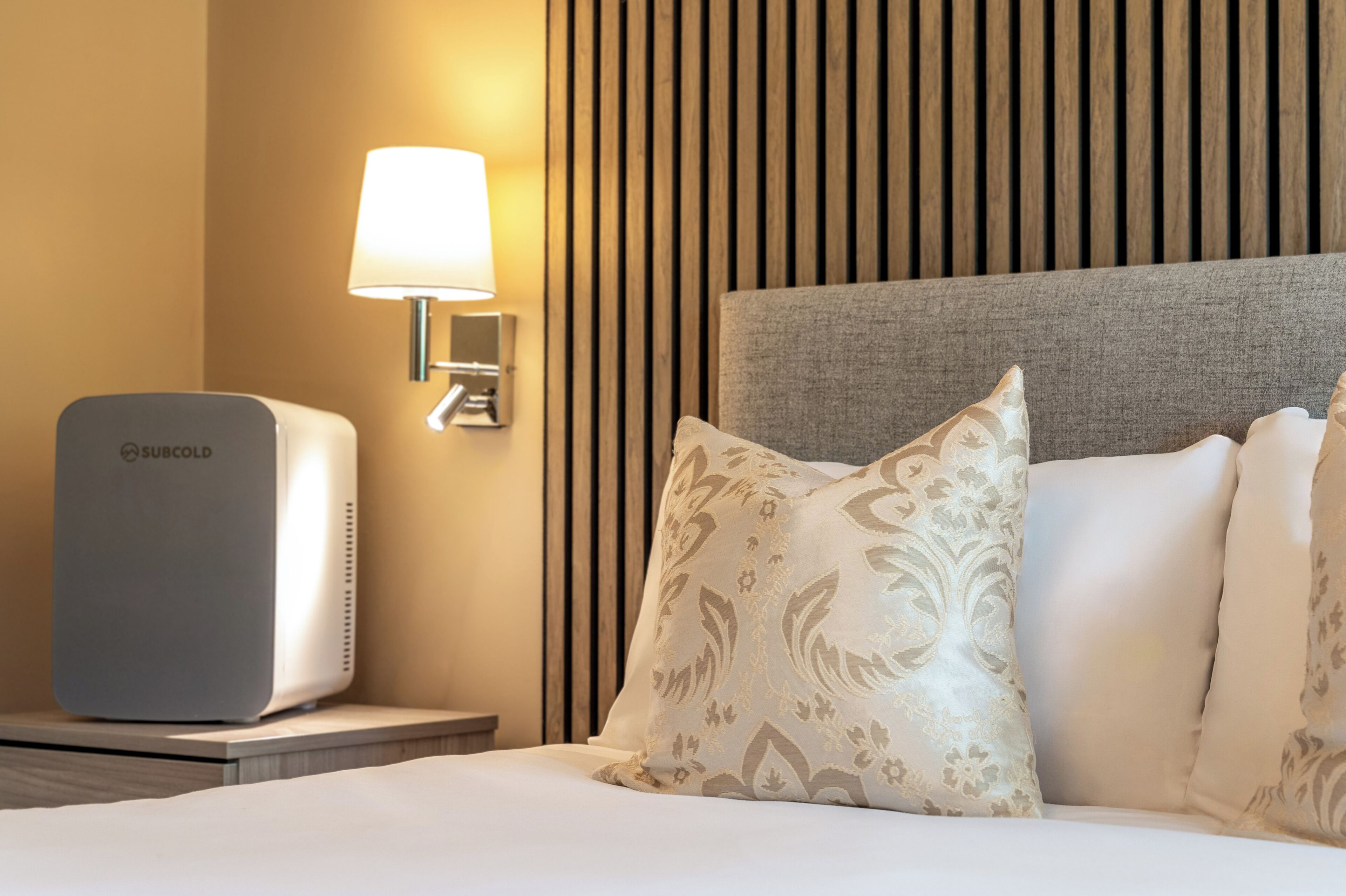 A hotel room with a bed, a wall-mounted lamp, and a minibar.