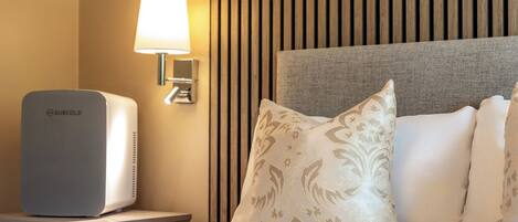 A hotel room with a bed, a wall-mounted lamp, and a minibar.