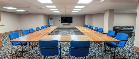 Una sala de conferencias con una larga mesa, sillas azules, una pantalla grande y alfombra estampada.