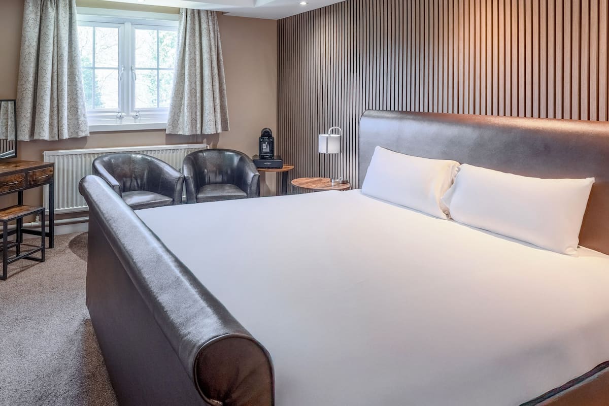 A hotel room with a large bed, two armchairs, a small table with a coffee maker, and a radiator.
