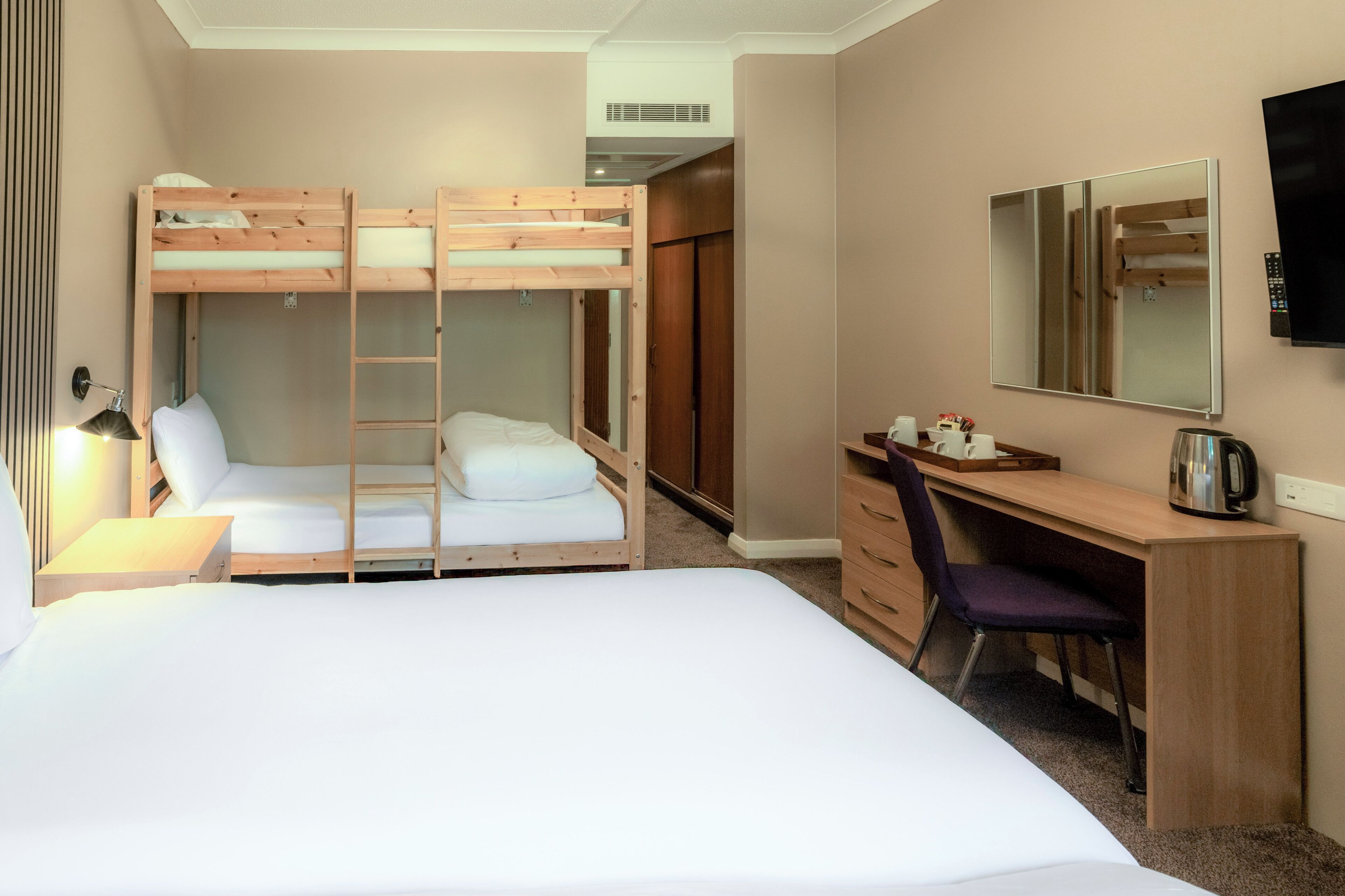 Un lit superposé avec un bureau et une chaise, un miroir et un téléviseur.