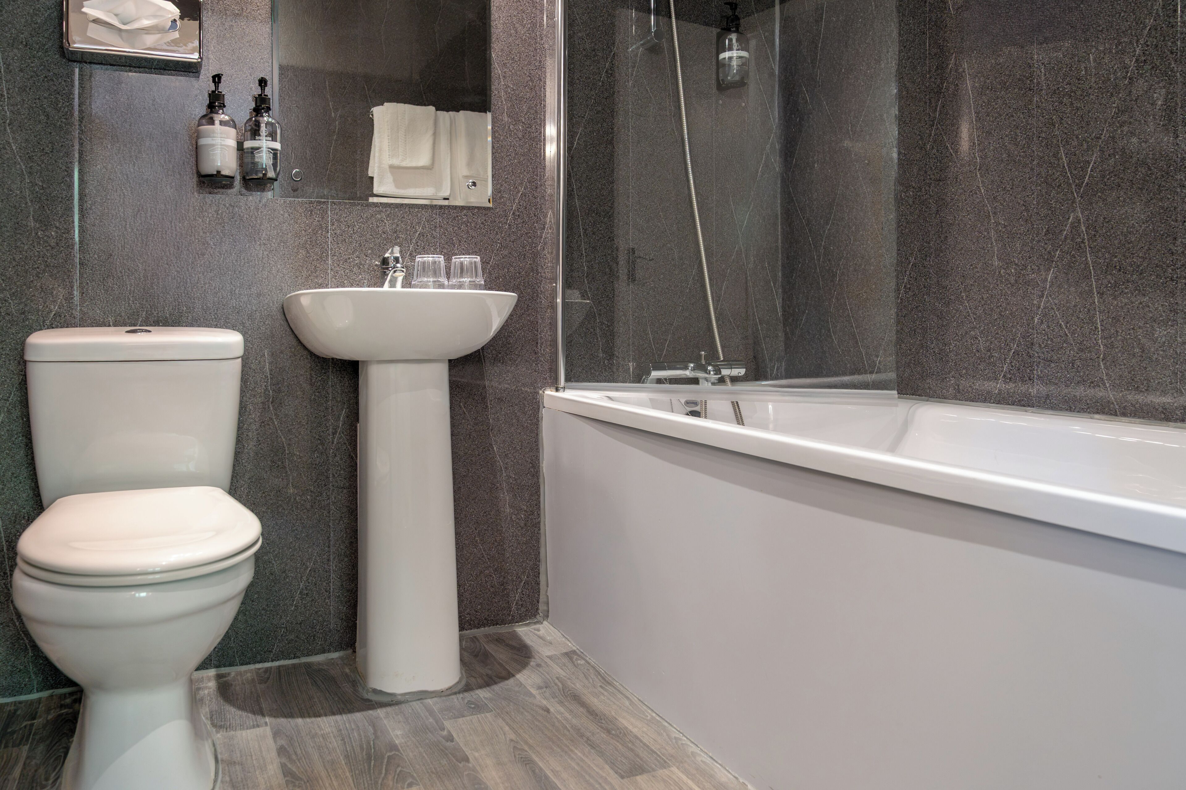 Une salle de bain moderne équipée de toilettes, d’un lavabo sur colonne et d’une baignoire.