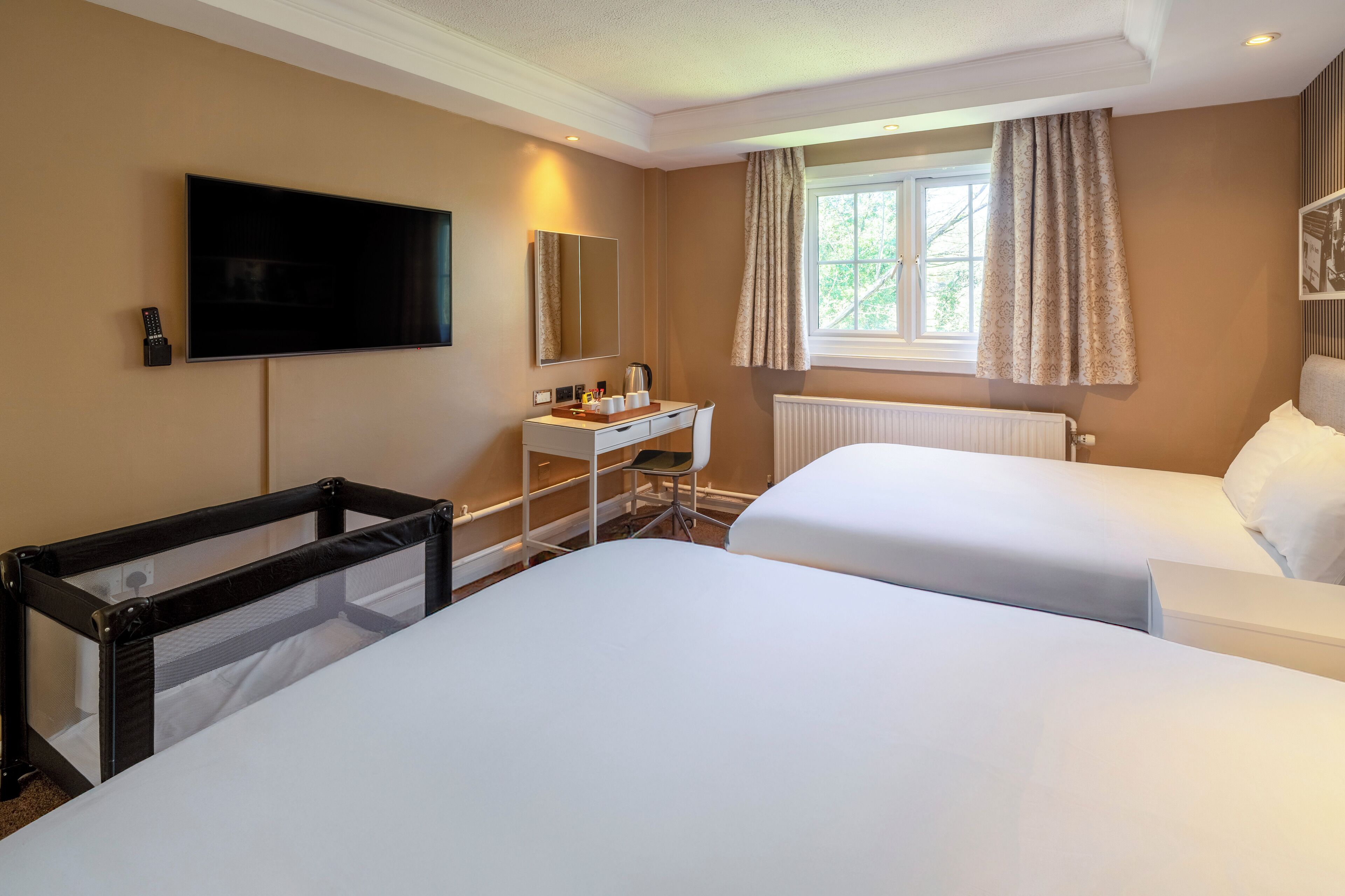 Ein Hotelzimmer mit zwei Betten, einem Fernseher, einem Schreibtisch mit Stuhl und einem Fenster mit Vorhängen.