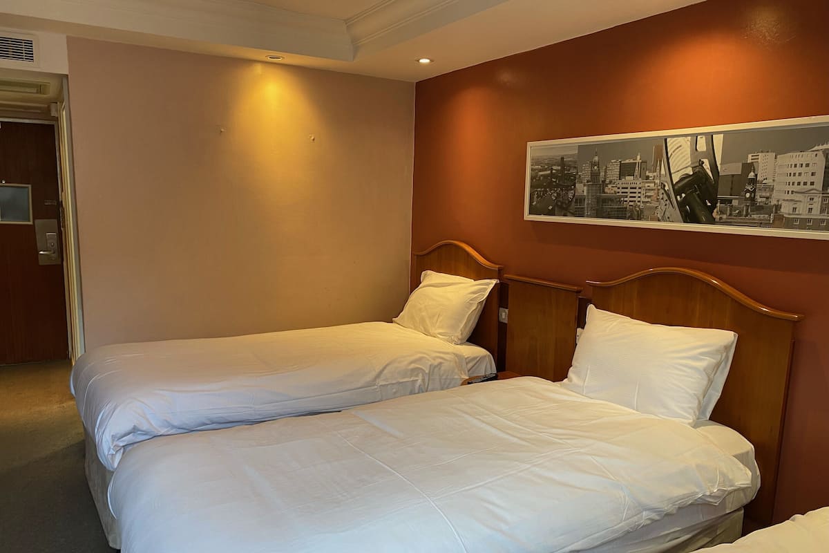 A hotel room with two single beds, a wooden headboard, and a cityscape painting on the wall.