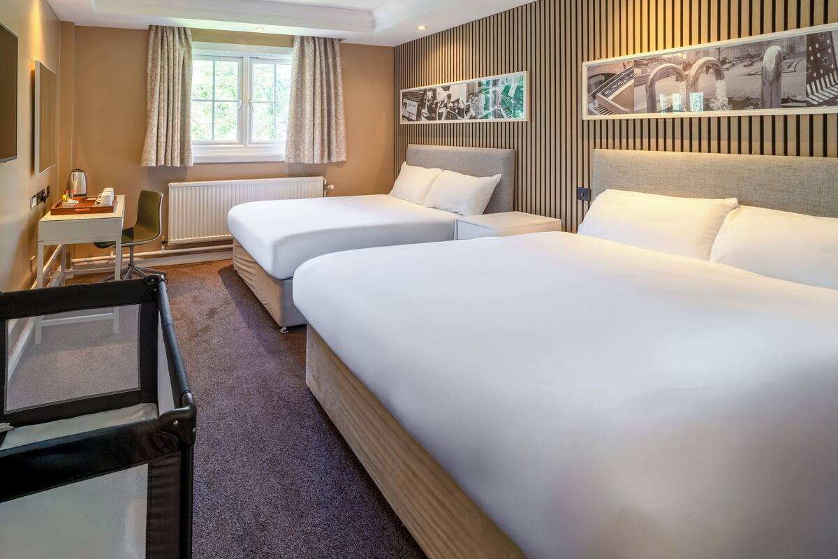 A hotel room with two single beds, a desk, a chair, and a radiator.
