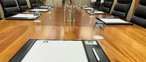 Una sala de conferencias con una larga mesa de madera, sillas de cuero negro y una pizarra.