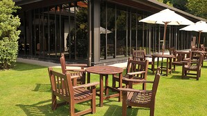 An outdoor patio with wooden tables and chairs, large umbrellas, and a glass enclosure in the background. - Britannia Airport Inn Manchester (Wilmslow)