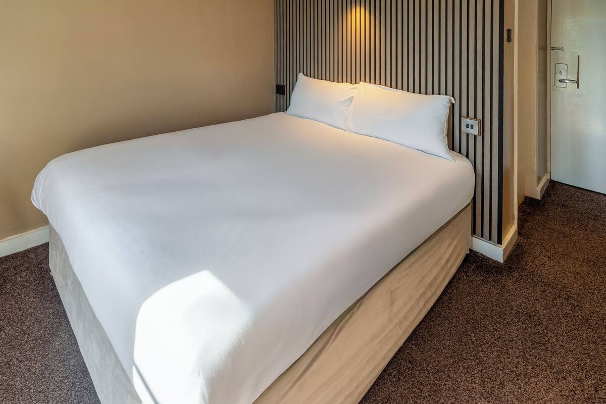 A neatly made bed with white linens in a hotel room.