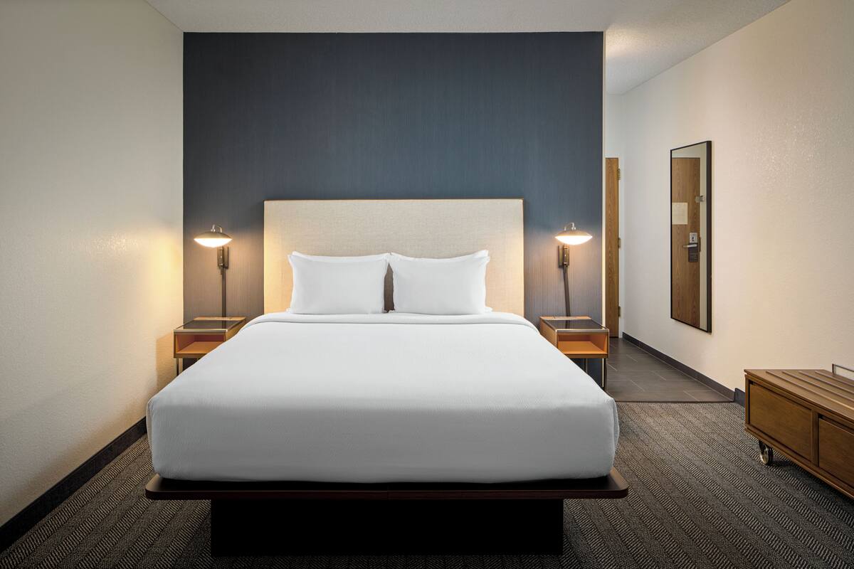 Ein Hotelzimmer mit einem großen Bett, zwei Nachttischen, einem Schminktisch und einem Teppichboden.