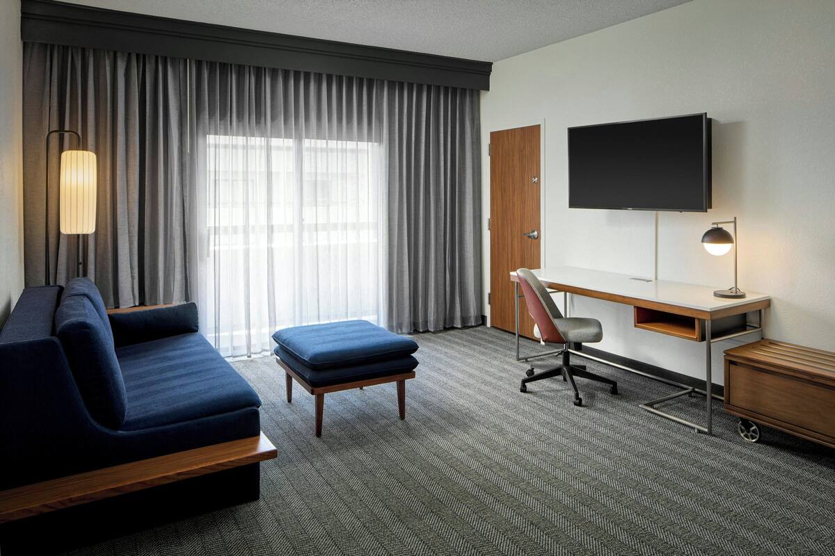 A hotel room with a sofa, a desk, a television, and a lamp.