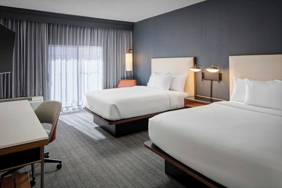 A hotel room with two beds, a desk, and a chair.