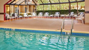 An indoor swimming pool with clear blue water, surrounded by white lounge chairs and a glass-enclosed area. - Courtyard by Marriott Manassas Battlefield Park (Manassas)
