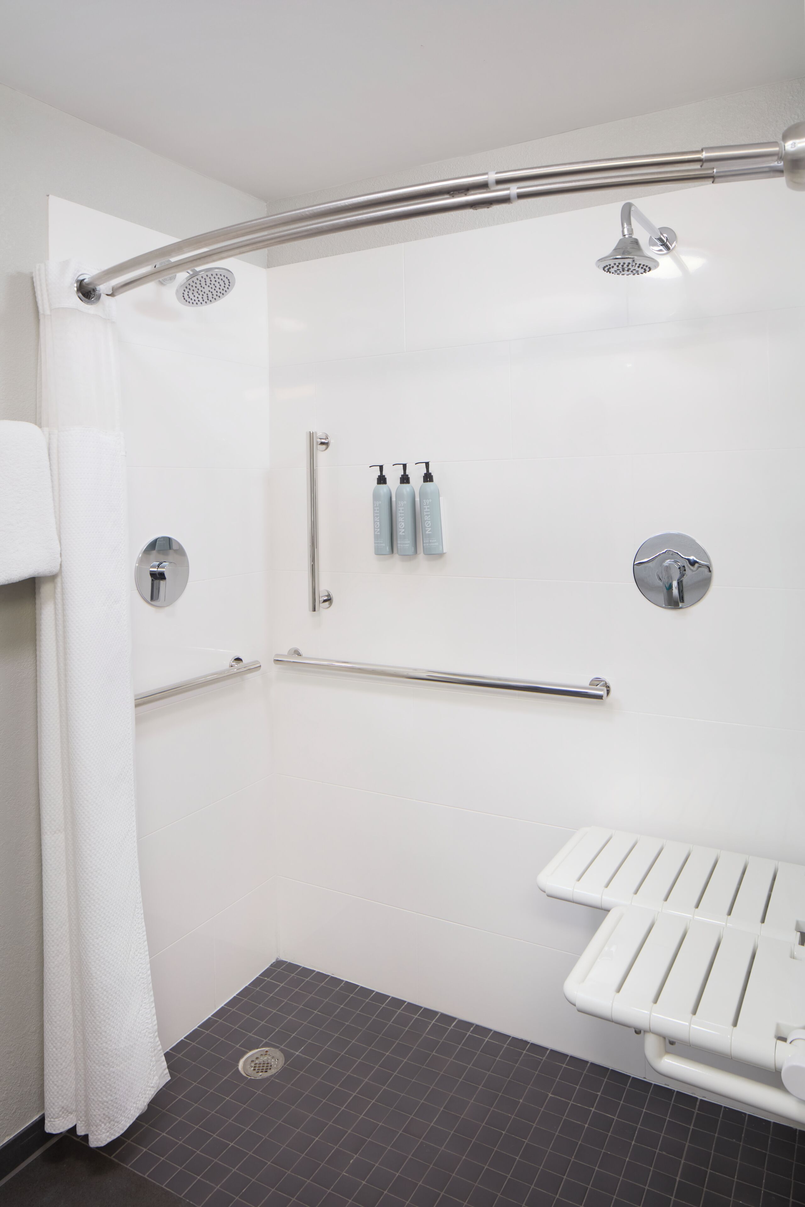 A modern bathroom with a shower, grab bars, a white sink, and a towel rack.