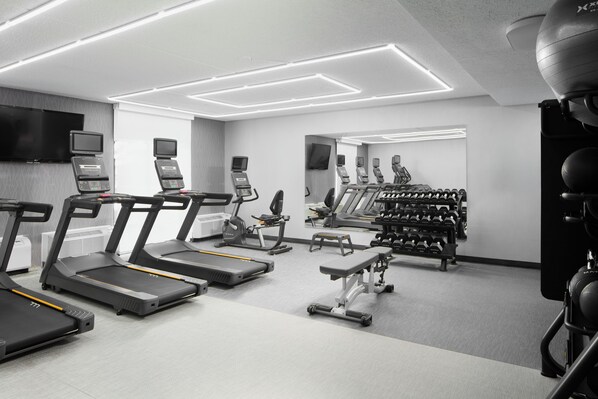 Un gimnasio moderno con cintas de correr, máquinas de pesas y un muro con espejos.
