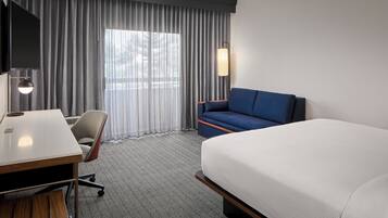 A hotel room with a bed, a desk, a chair, a TV, and a window with curtains.