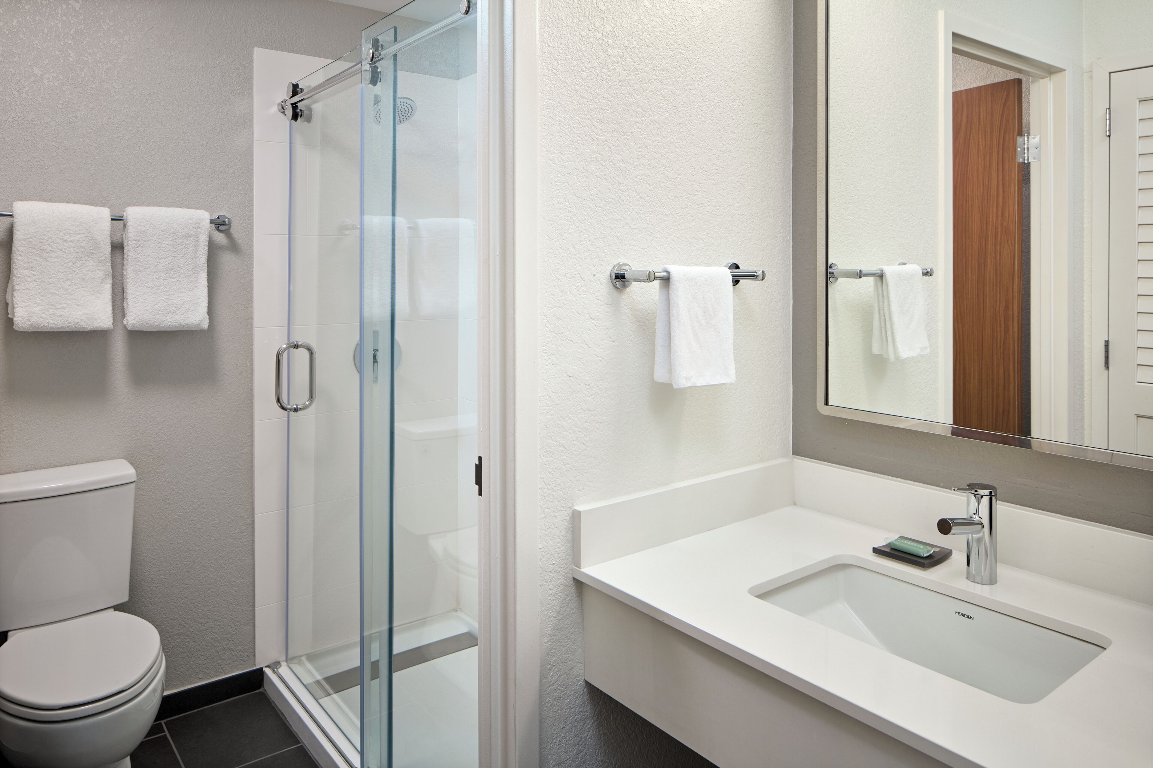 A modern bathroom with a glass shower enclosure, a white sink with a mirror, and two white towels on towel bars.